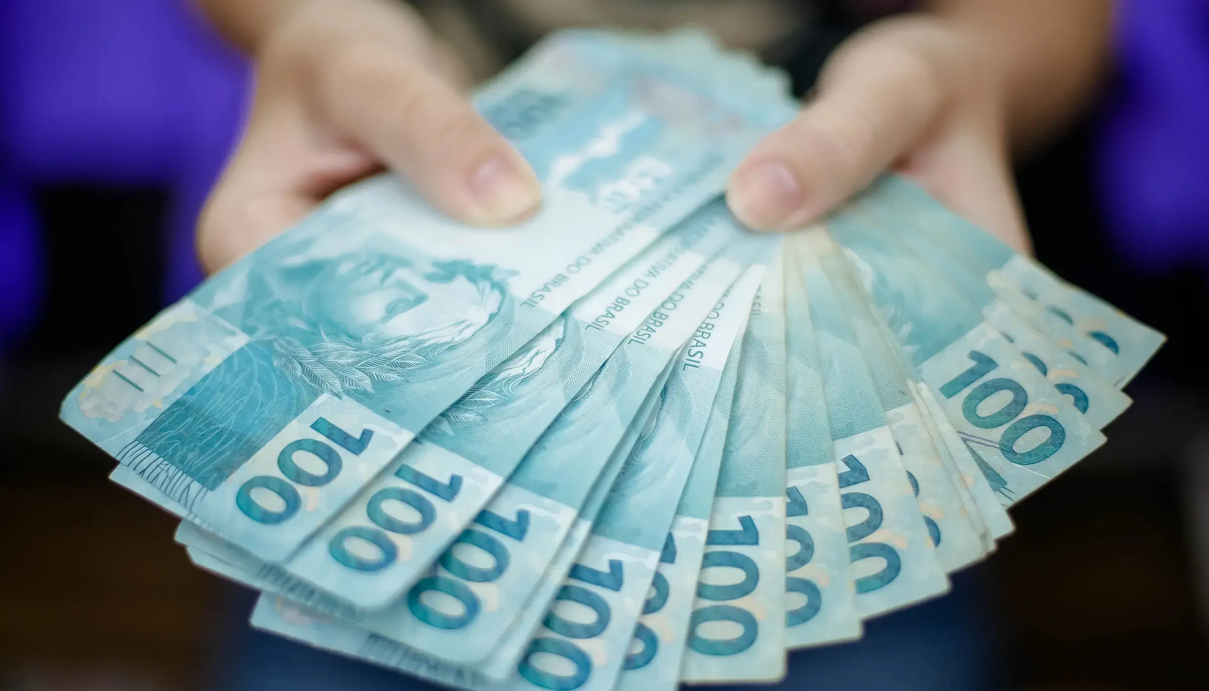 Mão segurando notas de 100 reais